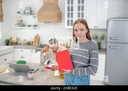 Fille à poil long en chemise grise portant un livre rouge Banque D'Images