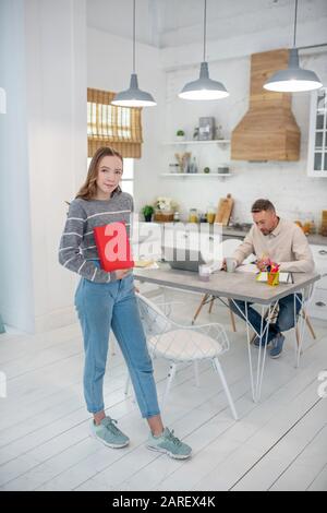 Fille à poil long en chemise grise montrant un livre rouge Banque D'Images