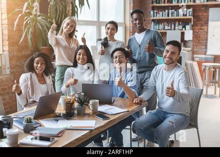Jeune équipe d'affaires joyeuse montrant pouce vers le haut Banque D'Images