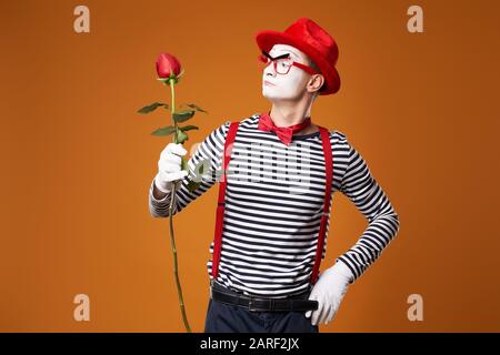 Mime sérieux dans Red Hat, verres et gilet avec rose dans les mains sur fond orange vide Banque D'Images