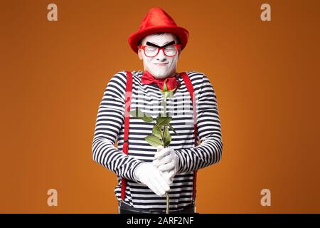 MIME avec Red Hat, lunettes et gilet avec rose en mains sur fond orange vide Banque D'Images