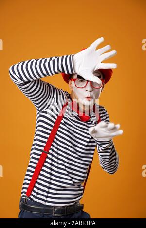 Mime sérieux dans des gants blancs et Red Hat regardant l'appareil photo sur fond orange vide Banque D'Images