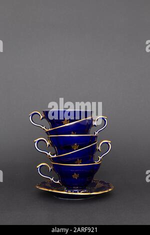 Gros plan de tasses à thé en porcelaine vintage bleu cobalt empilées avec motif fleuri doré sur fond gris foncé Banque D'Images
