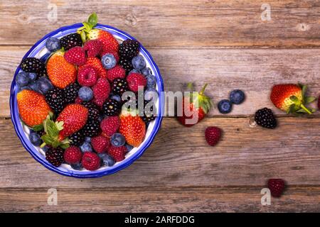 Vue de dessus d'un bol de fruits d'été, composé de fraises, framboises, bleuets et mûres, sur un vieux fond de bois. Gros plan Banque D'Images