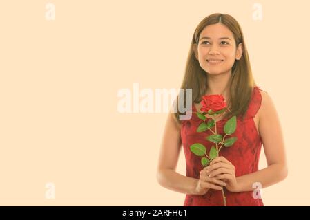 Thoughtful young woman smiling and holding red rose prêt pour la Saint-Valentin Banque D'Images