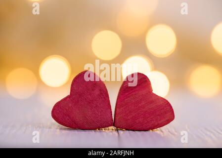 Contexte de la Saint Valentin. Deux coeurs rouges en bois avec des lumières bokeh en arrière-plan et espace de copie. Banque D'Images