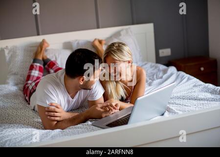 Les jeunes amoureux intime à l'aide d'ordinateur portable en position allongée sur le lit dans la chambre à coucher Banque D'Images