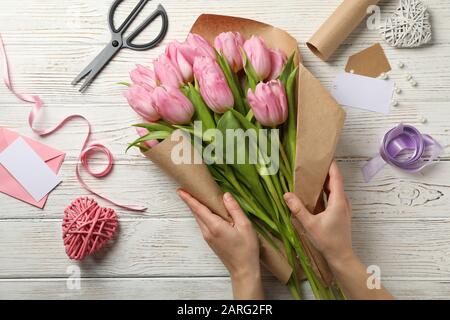 Girl emballe tulipes dans le papier d'artisanat sur fond en bois, vue de dessus Banque D'Images