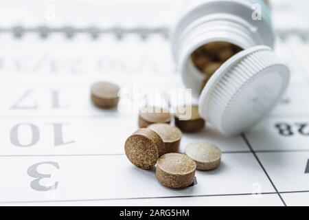Petites pilules sombres à côté d'un pot blanc ou une bouteille sur un fond de calendrier. Le traitement de la maladie. Santé Banque D'Images