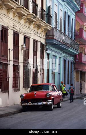 Scène de rue avec une vieille voiture rouge et des bâtiments usés à la Havane, Cuba. Banque D'Images