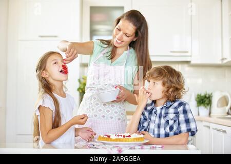 Deux enfants en collation avec leur mère tout en faisant cuire des gâteaux dans la cuisine Banque D'Images