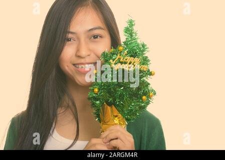 Studio shot of young happy Asian teenage girl smiling while holding Happy New Year tree Banque D'Images