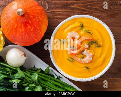 Délicieuse soupe à la crème de citrouille jaune avec crevettes et légumes sur fond en bois brun foncé, vue sur le dessus Banque D'Images