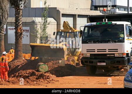 Tracteur de construction Caterpillar avec tombereau de chantier de chargement de creusement et travailleurs routiers devant le théâtre Joburg et d'autres bâtiments, Braamfontein, Banque D'Images