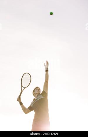 Un joueur de tennis masculin qui lance une balle pour le servir une journée ensoleillée. Le joueur de tennis sert une balle dans un match. Banque D'Images