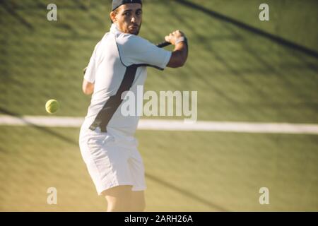 Un jeune joueur de tennis masculin frappe une main arrière puissante pendant un match. Joueur de tennis jouant au tennis sur un terrain de golf. Banque D'Images