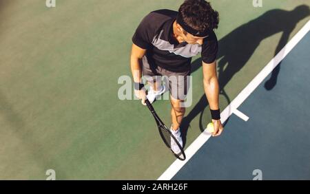 Vue de dessus d'un jeune joueur de tennis avec raquette prêt à servir une balle de tennis. Joueur professionnel debout à la base tenant la raquette de tennis et Banque D'Images