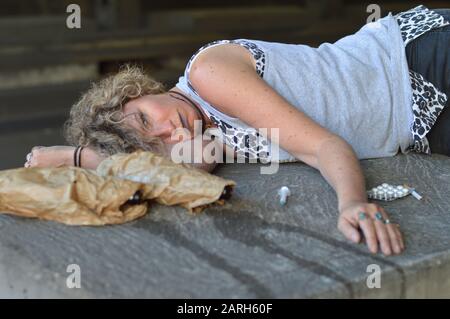 une femme sans abri ivre dormant sous un pont avec des bouteilles d'alcool et d'autres drogues autour d'elle Banque D'Images