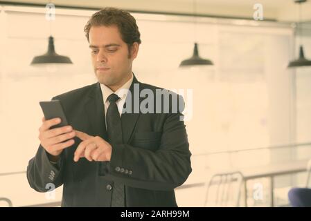 Homme d'affaires iranien en costume en utilisant le téléphone à la maison Banque D'Images