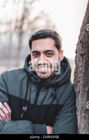 Portrait d'un jeune homme magnifique regardant un appareil photo et assis près d'un arbre Banque D'Images