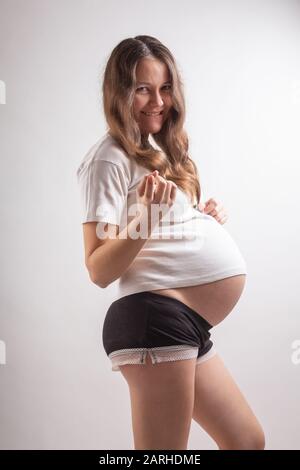 La jeune belle femme enceinte éprouve de fortes émotions sur un fond blanc Banque D'Images