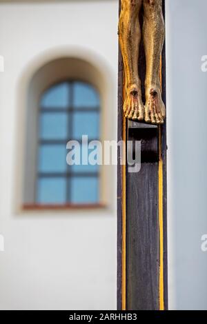 Vue partielle d'une croix chrétienne en bois, seulement les pieds du Christ, en arrière-plan la fenêtre d'une église Banque D'Images