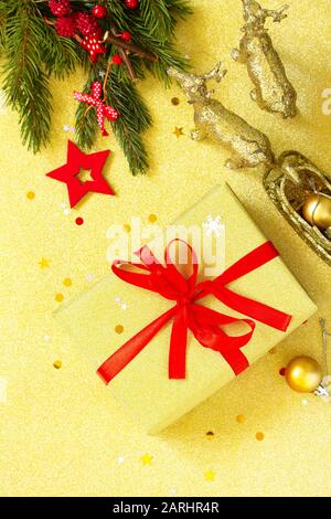 Boîte cadeau de noël à la main. Noël présente une boîte dorée avec ruban rouge et un décor de branche d'arbre. Vue de dessus sur un fond plat. Banque D'Images