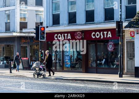 Une branche de café Costa à côté des feux de circulation avec une femme et une poussette traversant la route Banque D'Images