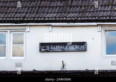 L'ancien panneau en bois pointant vers l'église paroissiale est fixé haut sur un mur de maison de ville juste en dessous du toit Banque D'Images