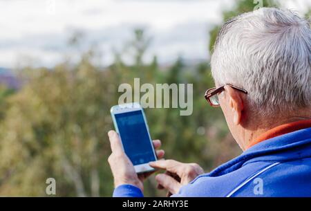 Vue arrière de l'homme âgé avec des lunettes prenant une photo avec le mobile Banque D'Images