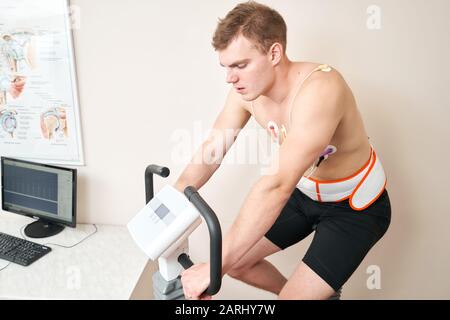 Homme patient, pédaler sur un système de test de stress ergomètre de vélo pour la fonction de coeur vérifiée. L'athlète effectue un test de stress cardiaque dans un médecin Banque D'Images