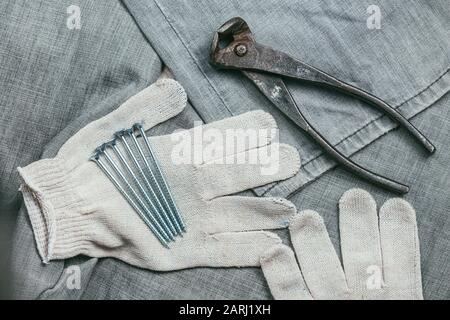 Une poignée de vis auto-coupantes métalliques et de pinces très anciennes et rouillées se trouvent sur les gants de travail tricotés de sécurité pour une utilisation industrielle sur fond de Banque D'Images