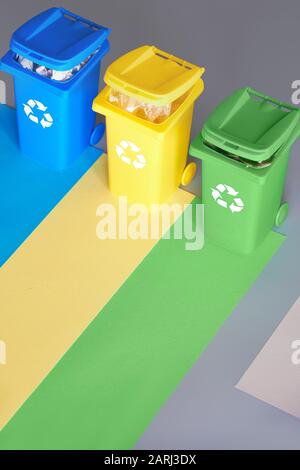 Trois bacs de recyclage à code couleur, image isométrique sur fond de papier superposé géométrique. Panneau de recyclage sur les bacs bleu, jaune et vert. Déchets separati Banque D'Images