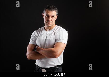 Beau Athletic homme en t-shirt blanc vierge debout sur fond de mur noir Banque D'Images