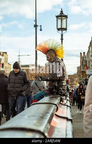 Londres / Royaume-Uni - 01 décembre 2019: Tatoed face punk avec mohawk coloré assis sur la rue à Camden Town. La sous-culture punk est apparue dans le Kin Uni Banque D'Images