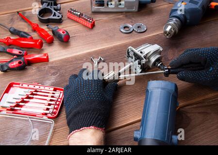 Le maître à réparer un appareil électrique cassée : perceuse, cutter sur une table en bois. Atelier de réparation d'outils électriques Banque D'Images