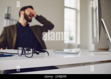 Un travailleur fatigué épuisé sur le lieu de travail a couvert son visage avec ses mains au bureau Banque D'Images