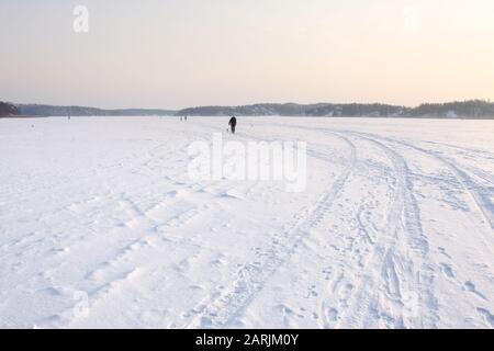 Les gens marchant sur une épaisse mer gelée recouverte de neige. Le soleil s'enfonce lentement. Banque D'Images