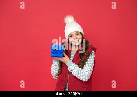 faites des choses agréables. joyeux enfant en hiver avec fond rouge. nouvelle année à venir. petit coffret cadeau pour enfant. bonne enfance. cadeaux de noël et souvenirs. préparez-vous pour les vacances d'hiver. Banque D'Images