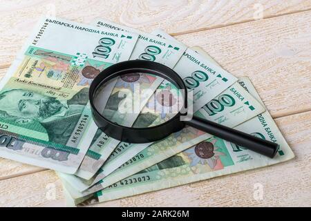 Billets et loupe bulgares de 100 lev sur une surface en bois blanc. Vérifiez l'authenticité de l'argent. Concept de richesse, de pauvreté et de contrefaçon de monnaie Banque D'Images