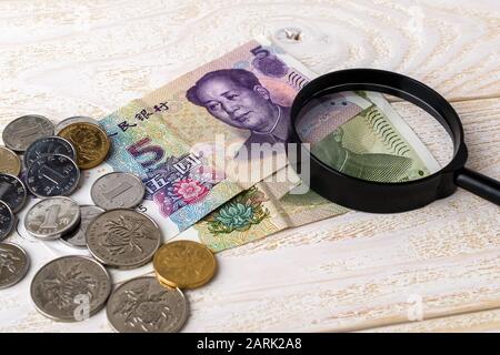 Loupe sur les billets et pièces de yuan chinois sur une surface en bois blanc. Vérifiez l'authenticité de l'argent. Richesse, pauvreté et contrefaçon. Banque D'Images