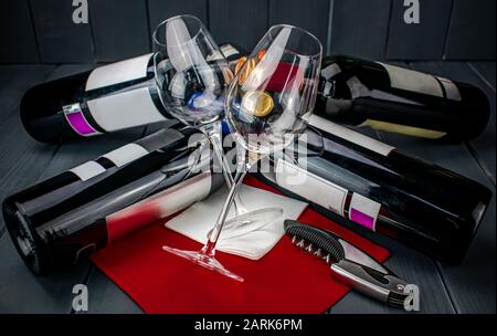 Deux verres à vin lumineux se trouvant sur plusieurs bouteilles de vin rouge et un tire-bouchon, sur la nappe rouge, dans un espace en bois gris bien éclairé Banque D'Images