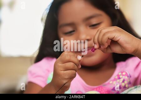 Une jolie petite fille qui s'amuse tout en créant des bijoux de perles à l'aide de cordes et de perles colorées. Banque D'Images