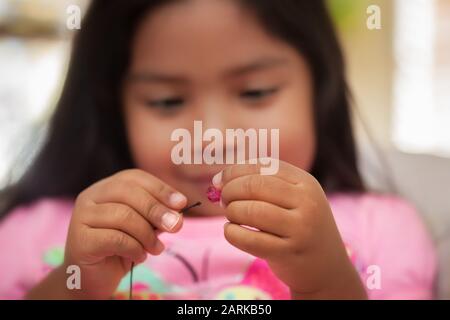 Un enfant améliore ses compétences en matière de moteur fin en utilisant une poignée de pincer tout en tenant des cordes et des perles. Banque D'Images