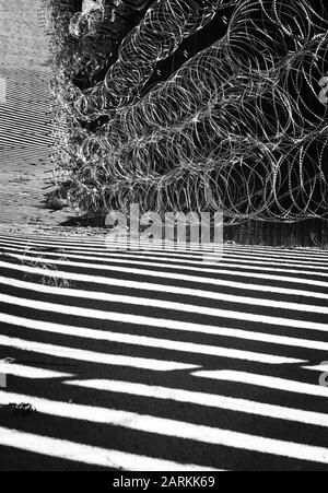 Vue abstraite de la barrière de la frontière internationale entre les États-Unis et le Mexique avec un fil de rasoir avec une lumière et des ombres spectaculaires à Nogales, AZ, USA, en noir et blanc Banque D'Images