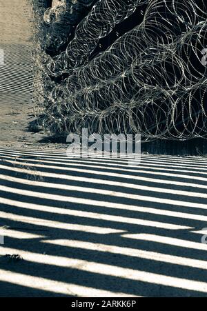 Vue abstraite de la barrière de la frontière internationale entre les États-Unis et le Mexique avec un fil de rasoir avec une lumière et des ombres spectaculaires à Nogales, AZ, USA, en noir et blanc Banque D'Images