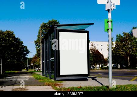 abri de bus structure en verre le long du trottoir de la rue. arbres verdoyants. scène estivale. panneaux publicitaires blancs. espace publicitaire. espace de copie de panneaux publicitaires blancs Banque D'Images