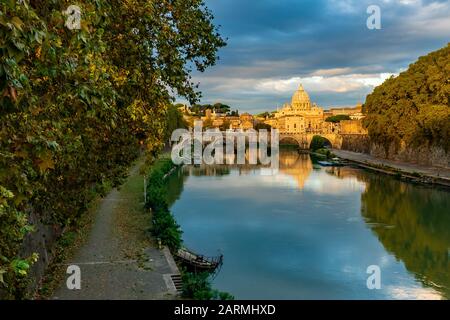 Vue sur le dôme de la basilique Saint-Pierre à Rome depuis un pont au-dessus du Tibre au coucher du soleil avec des couleurs et des reflets fantastiques dans l'eau, en Italie Banque D'Images