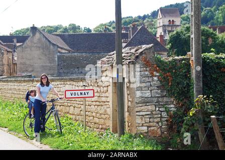 Une mère et un rire à vélo le long de la piste cyclable de la Côte de Beaune s'interrompont à côté du panneau pour Volnay Banque D'Images