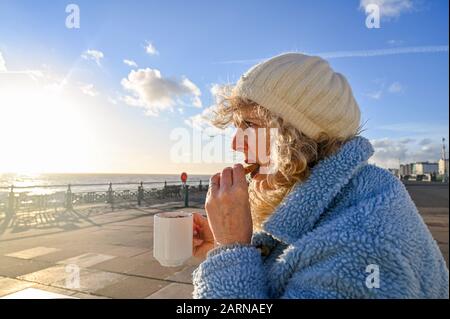 Une femme mûre d'âge moyen qui aime une tasse de café et de biscuit dans un café en bord de mer de Brighton le jour ensoleillé de l'hiver Banque D'Images